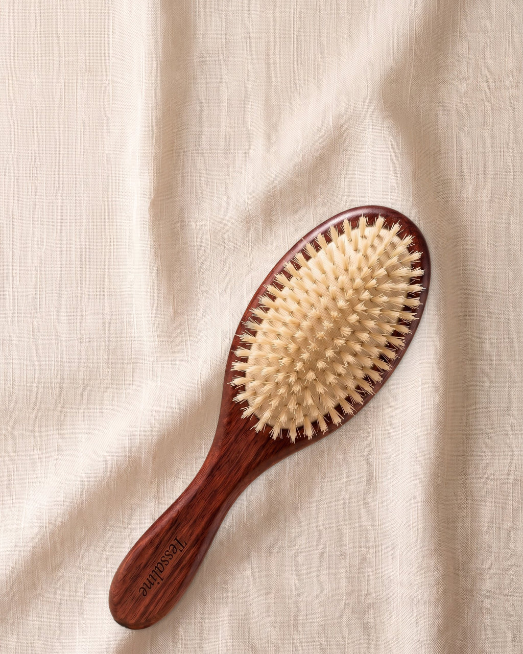 The Soft Grade boar bristle brush with a wooden handle, bristles facing up, on natural linen