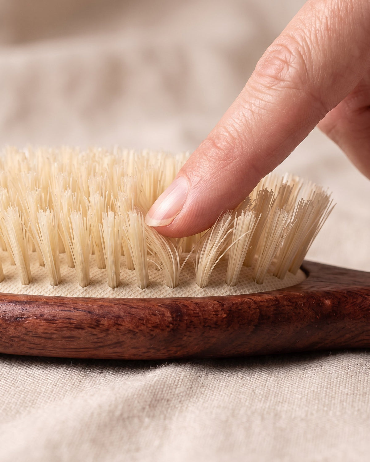 A fingertip pressing on soft boar bristle tufts, which bend under light pressure