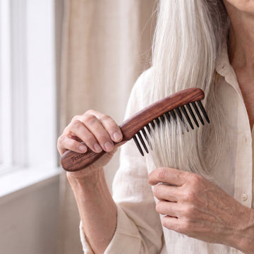 Hands using a wide-tooth comb on the ends of fine, dry silver hair