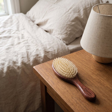 The Soft Grade brush on a bedside table next to a linen lamp